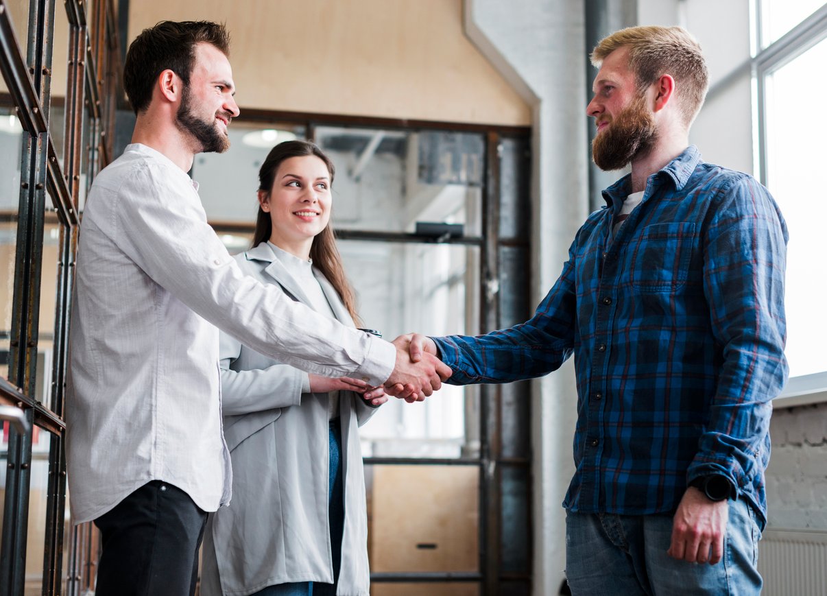 companero-trabajo-masculino-dos-que-sacude-mano-delante-empresaria-sonriente-oficina