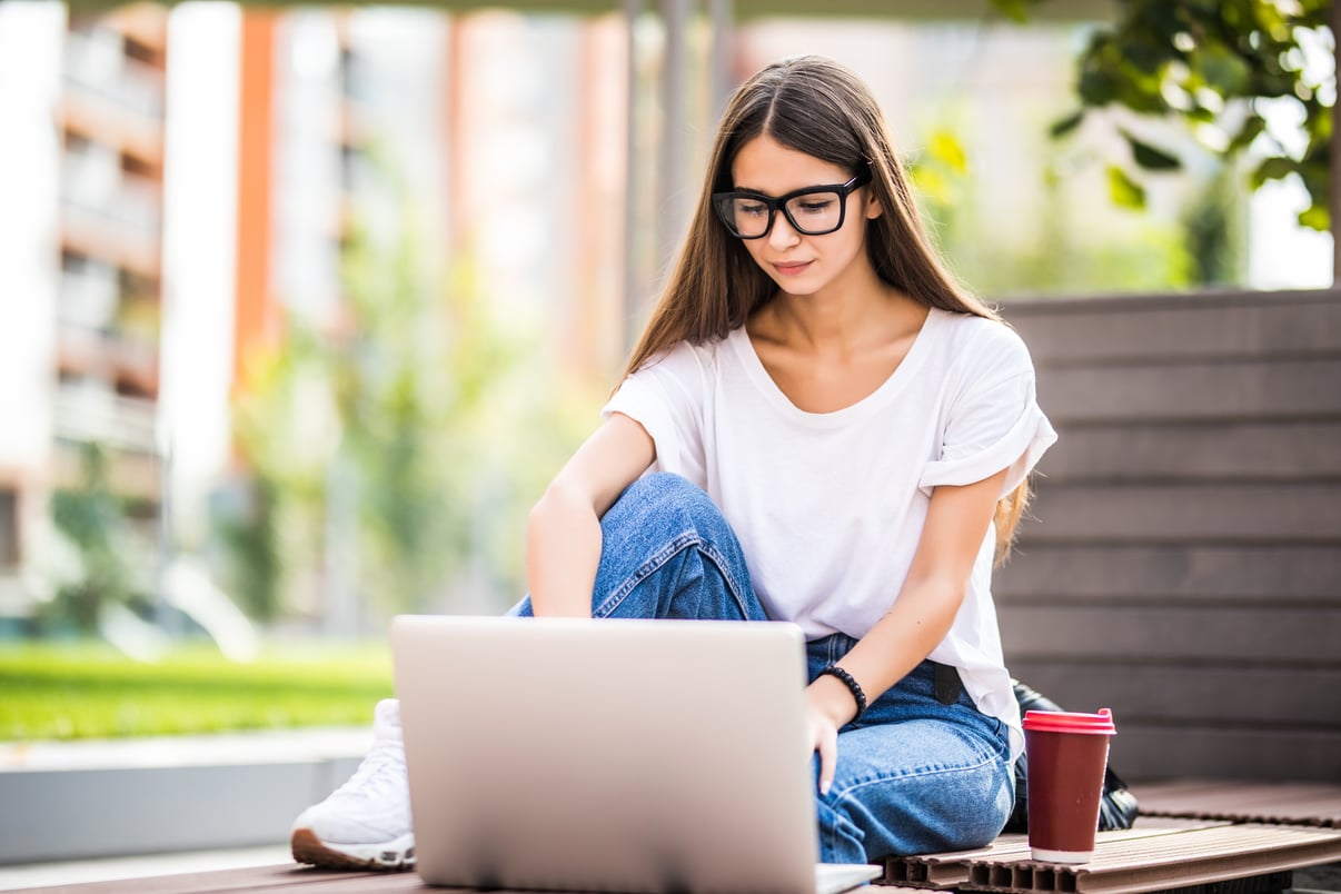 hermosa-joven-usando-laptop-mientras-sentado-banco-bebiendo-taza-cafe-llevar
