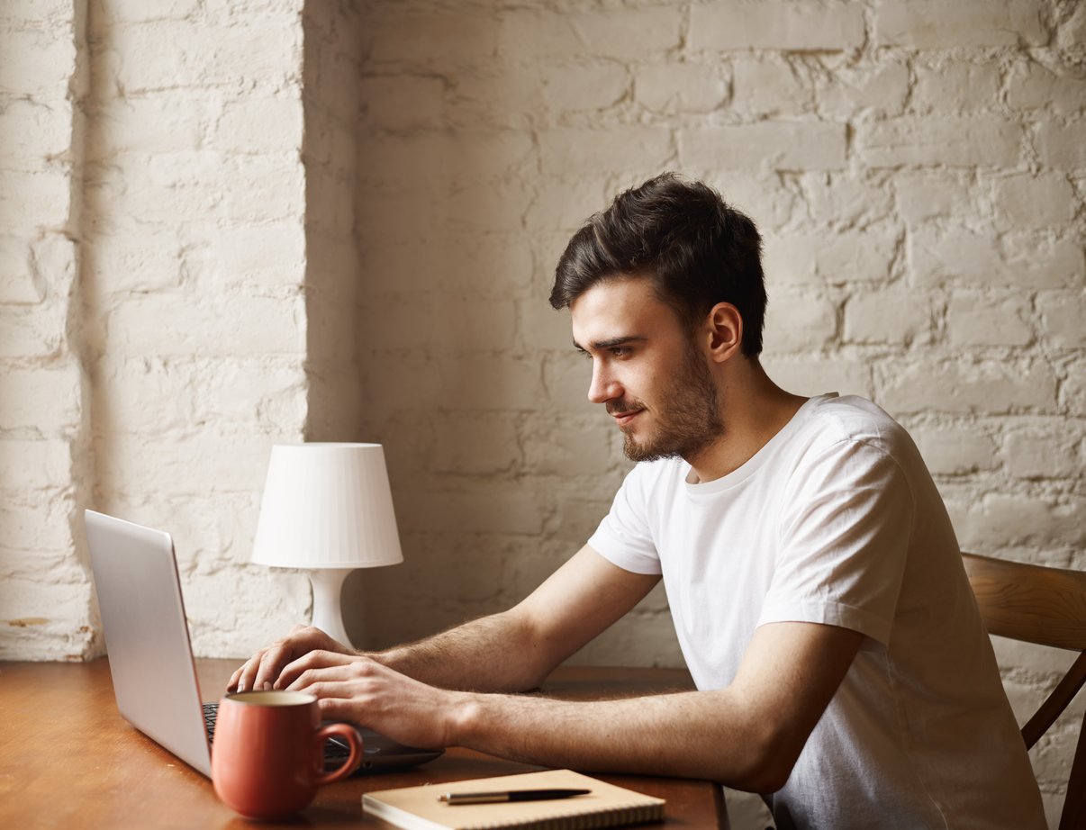 hipster-feliz-camiseta-blanca-sentarse-debajo-mesa-escribir-mensaje-cuaderno-amiga
