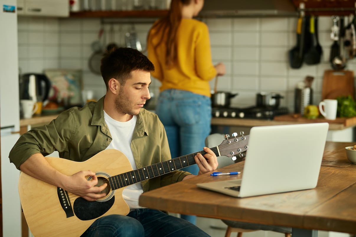 joven-tocando-guitarra-acustica-mientras-su-esposa-prepara-comida-fondo