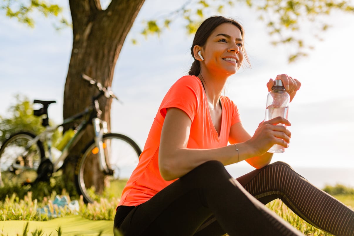 sonriente-mujer-hermosa-bebiendo-agua-botella-haciendo-deporte-manana-parque